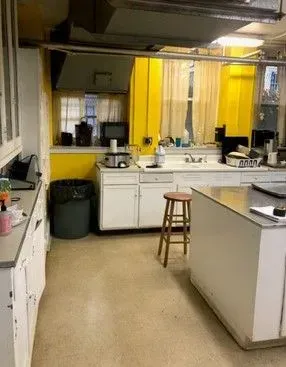 A kitchen with yellow walls and white cabinets and a stool.