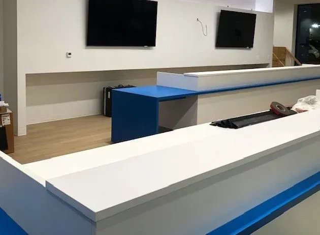 A white and blue counter in a room with two televisions on the wall.