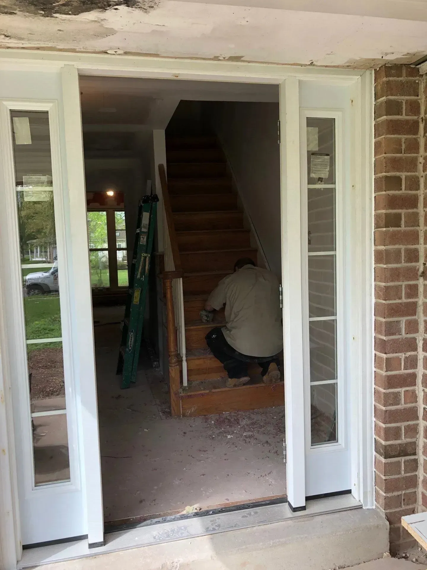 A man is kneeling down in front of a staircase in a house.