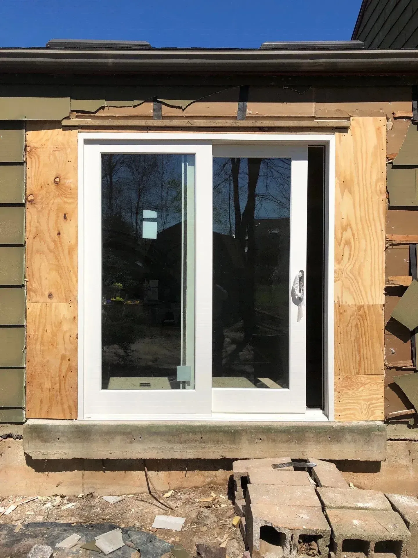 A white sliding glass door is being installed on the side of a house.