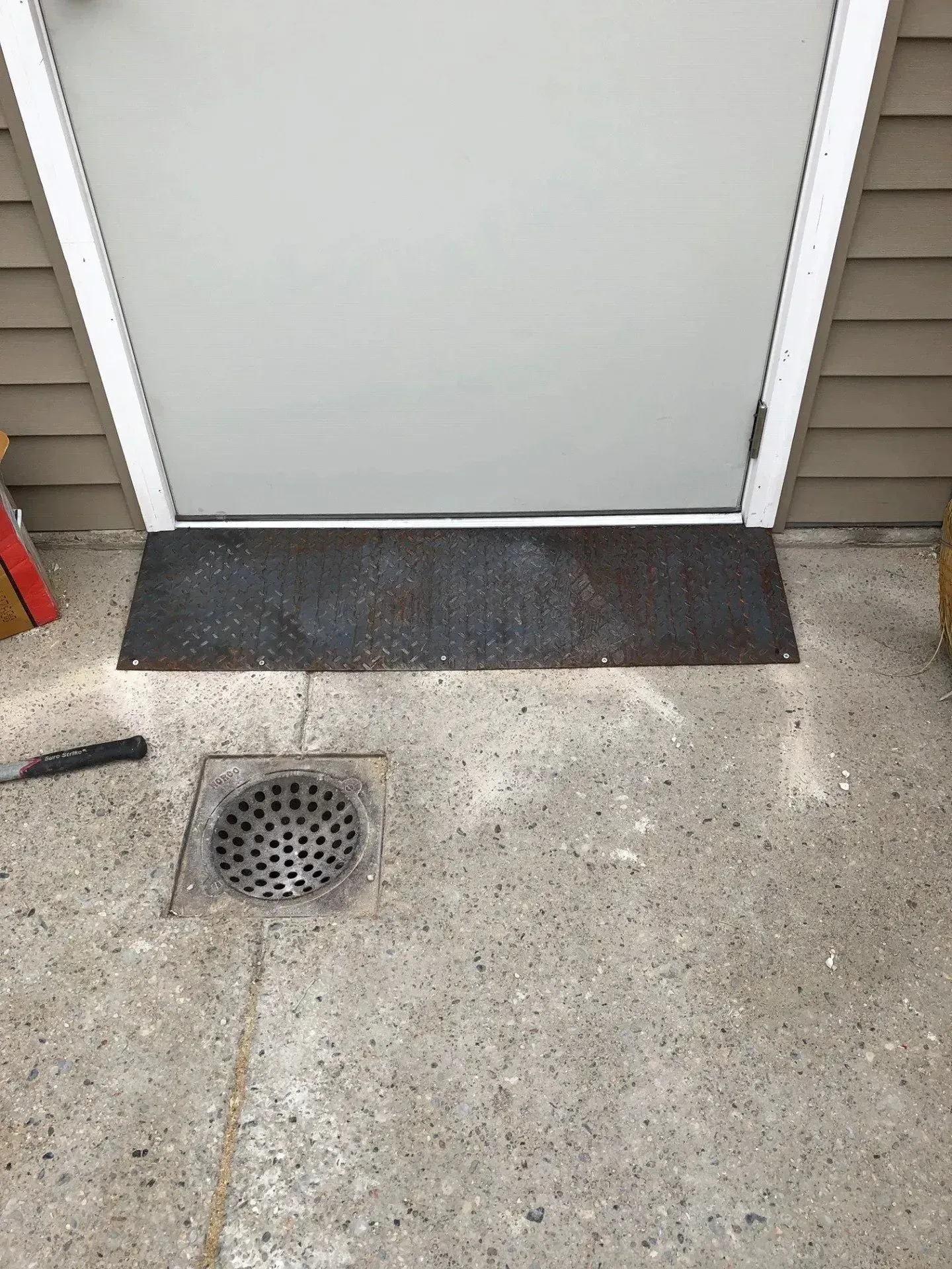 A white door is sitting on a concrete floor next to a drain.
