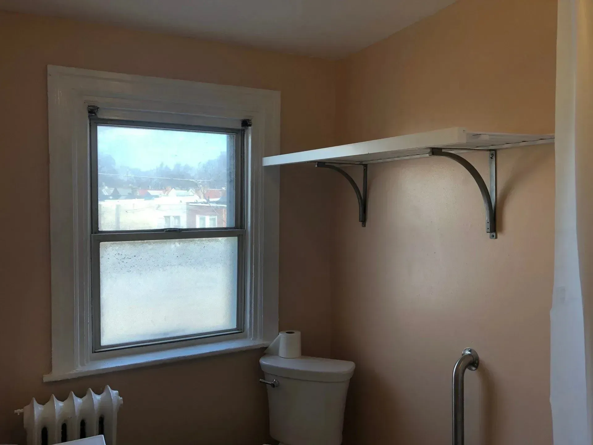 A bathroom with a toilet a window and a shelf
