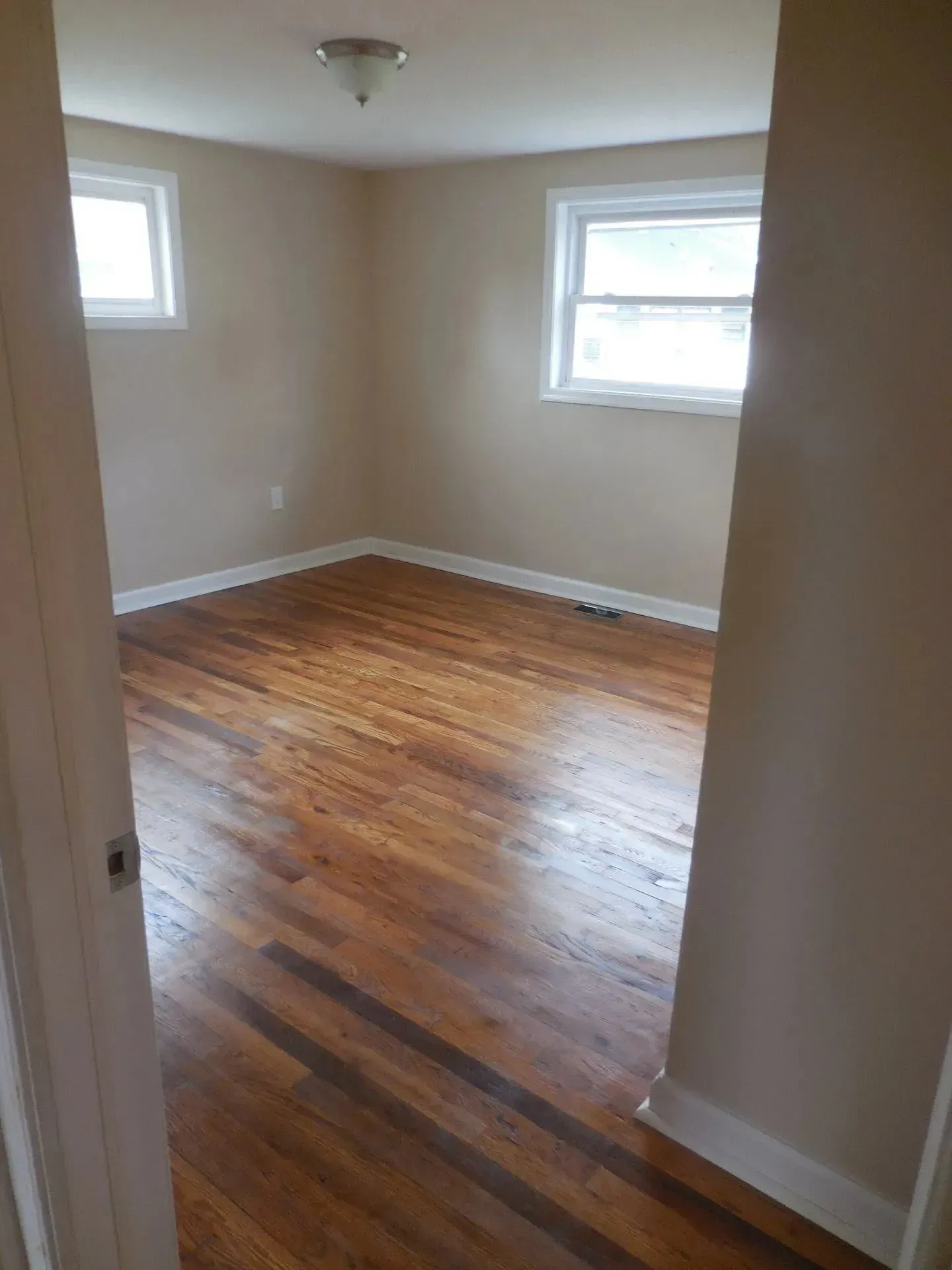 An empty room with hardwood floors and two windows.