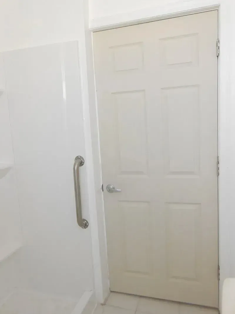 A bathroom with a white door and a stainless steel handle
