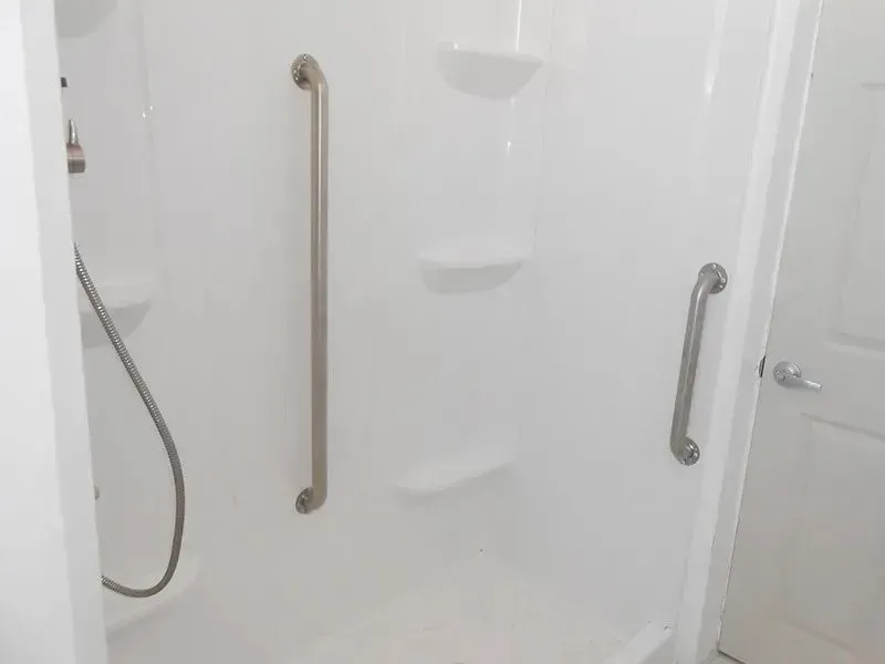 A white shower stall with stainless steel handles and shelves.