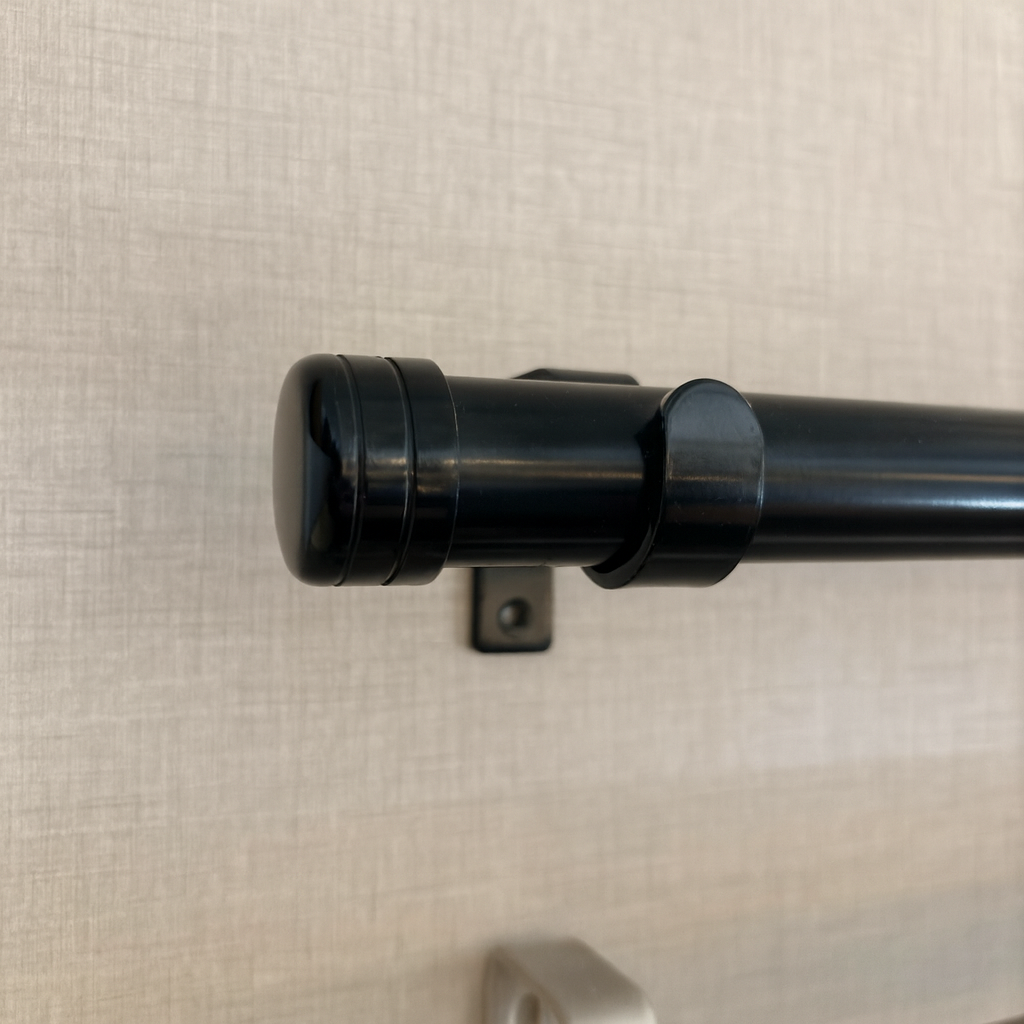 Barra de cortina de color negro con extremo redondeado y soporte montado en una pared de color claro.