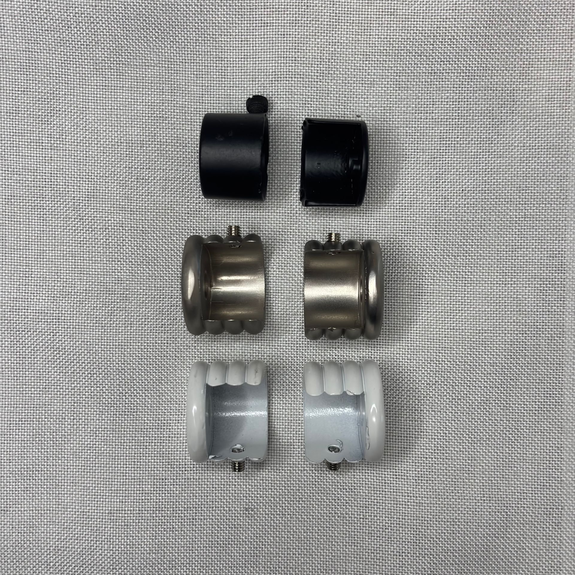 Seis piezas surtidas de herrajes para barras de cortinas, de color negro, plateado y blanco, sobre tela gris.