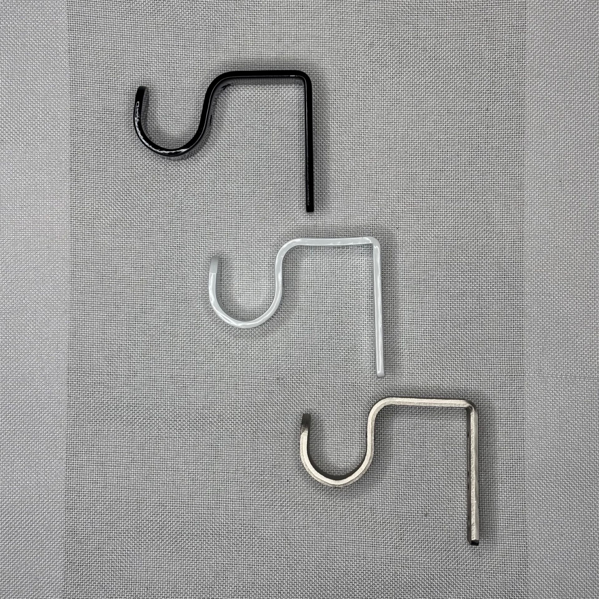 Tres ganchos de pastor de metal: negro, blanco y dorado, sobre una superficie gris texturizada.