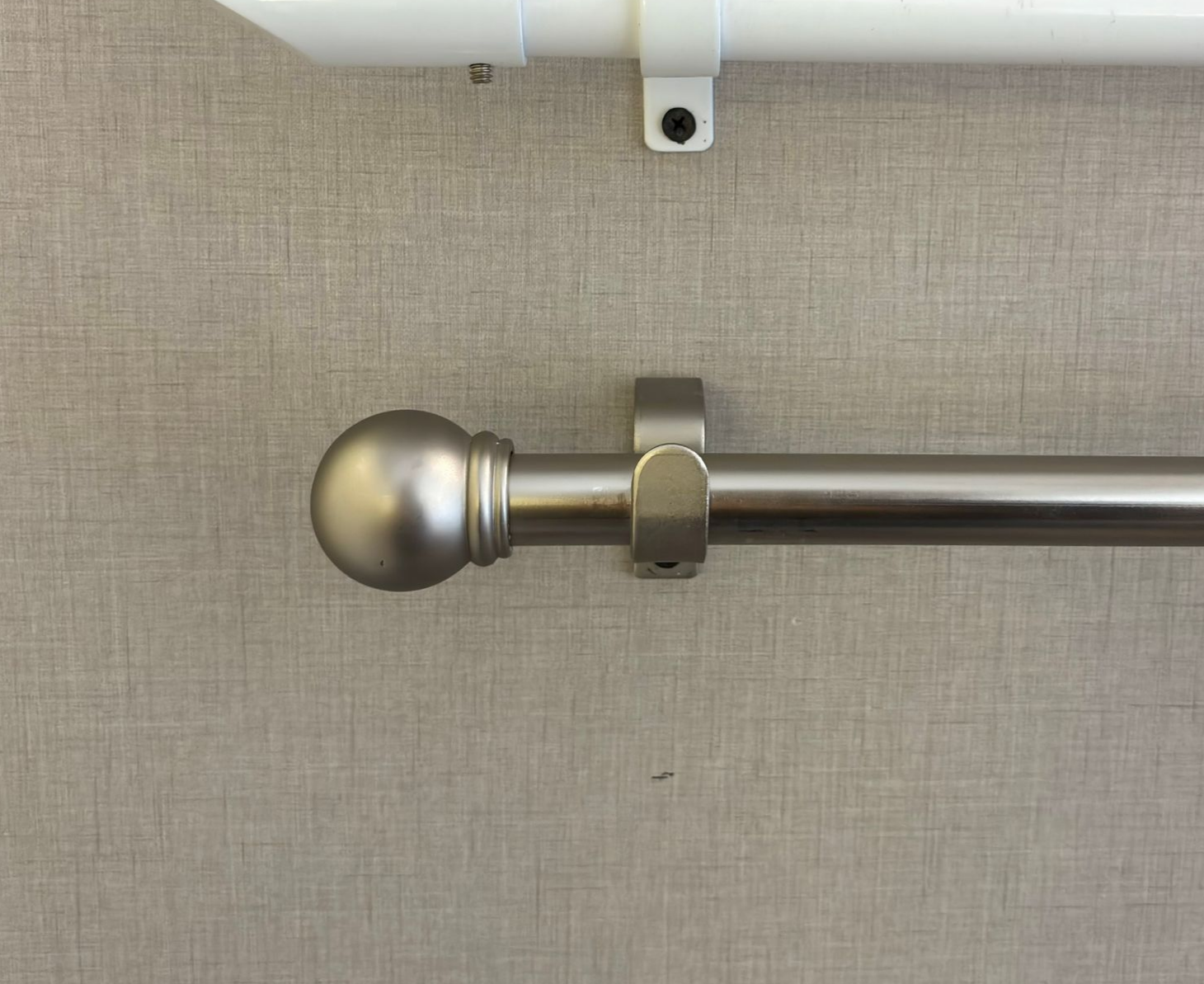 Dos remates esféricos de barra de cortina plateados sobre una superficie blanca.