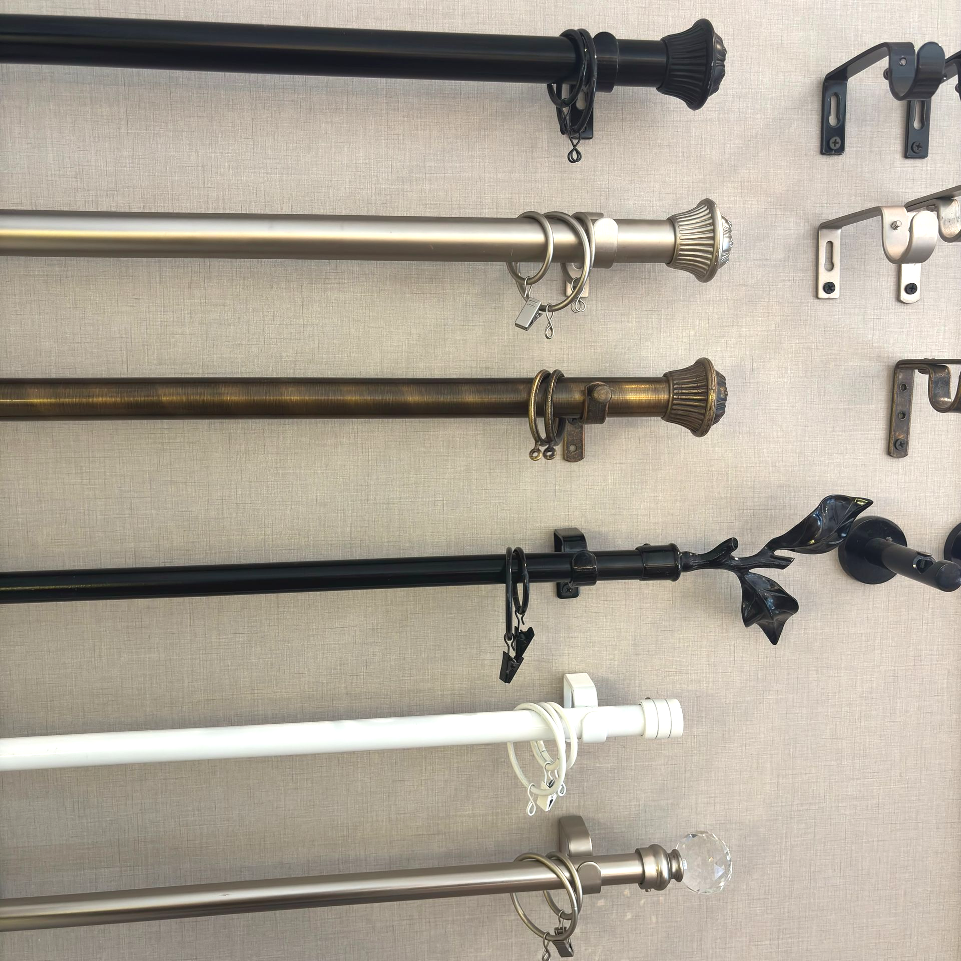 Tres barras de cortina, de color bronce, negro y blanco, montadas en una pared beige.
