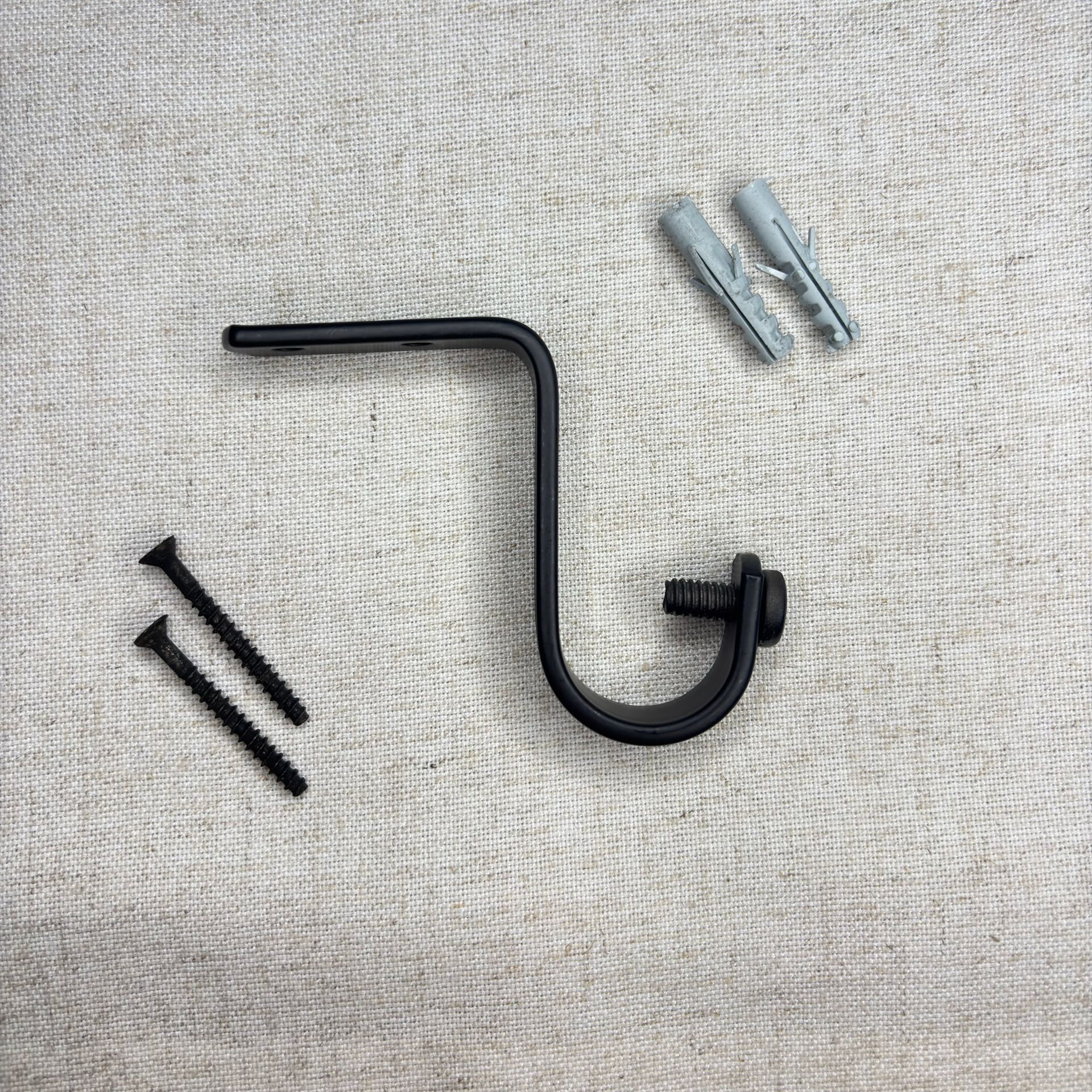 Soporte de barra de cortina negro con tornillos y anclajes de pared sobre una superficie texturizada.