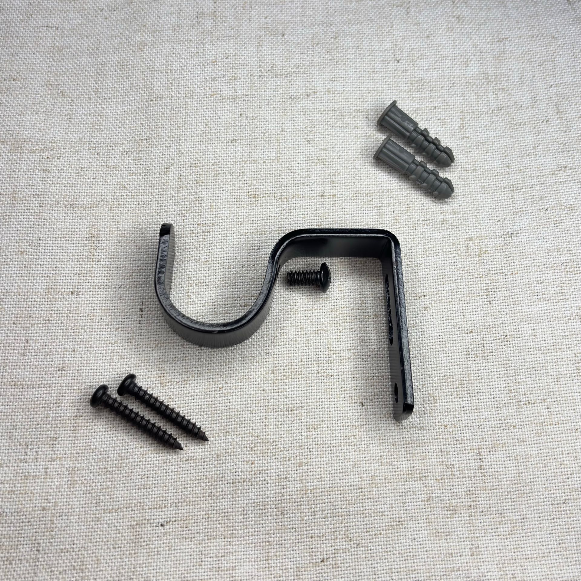 Soporte de barra de cortina negro con tornillos y anclajes de pared sobre una superficie gris texturizada.