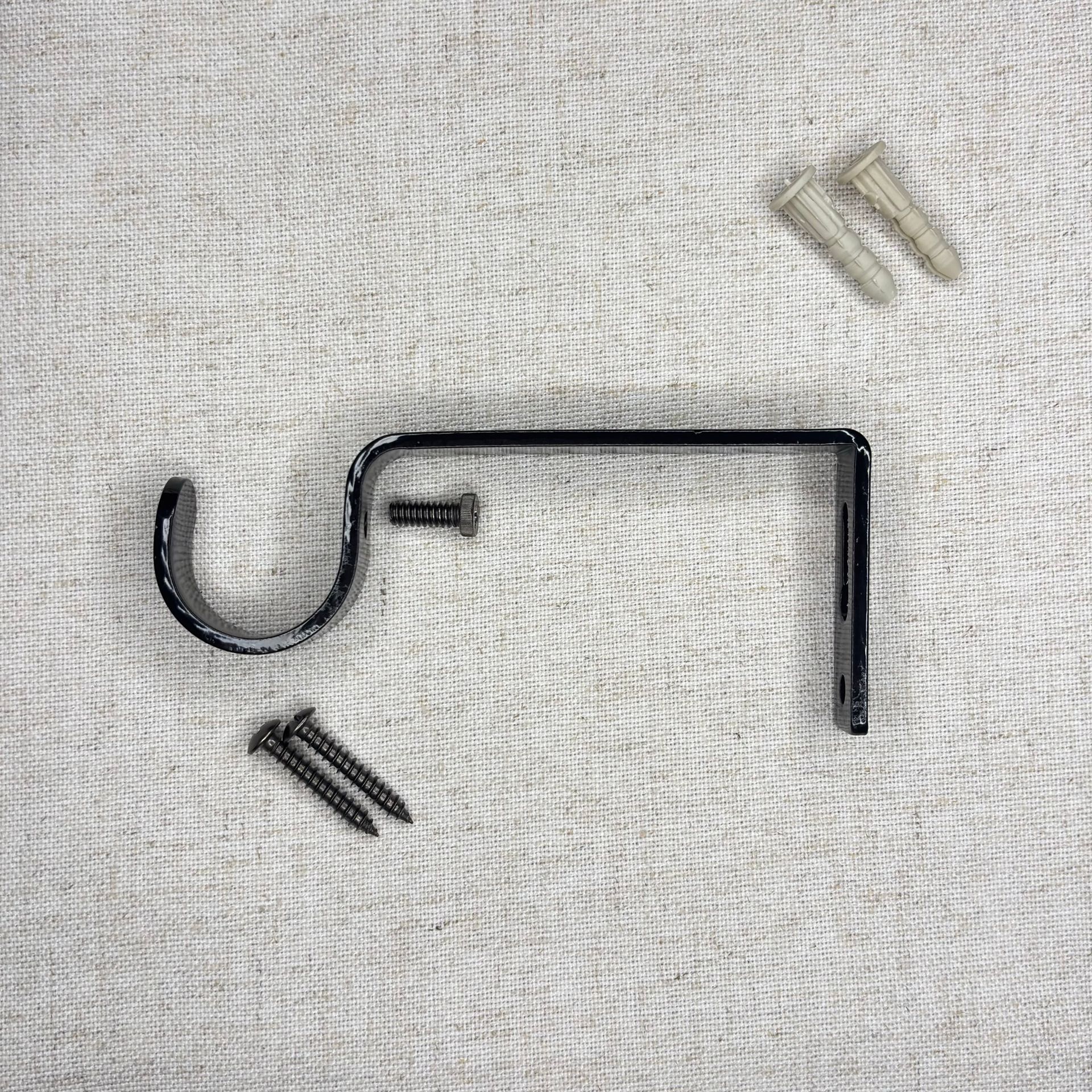 Soporte de barra de cortina de metal negro con tornillos y anclajes de pared sobre una superficie texturizada blanca.