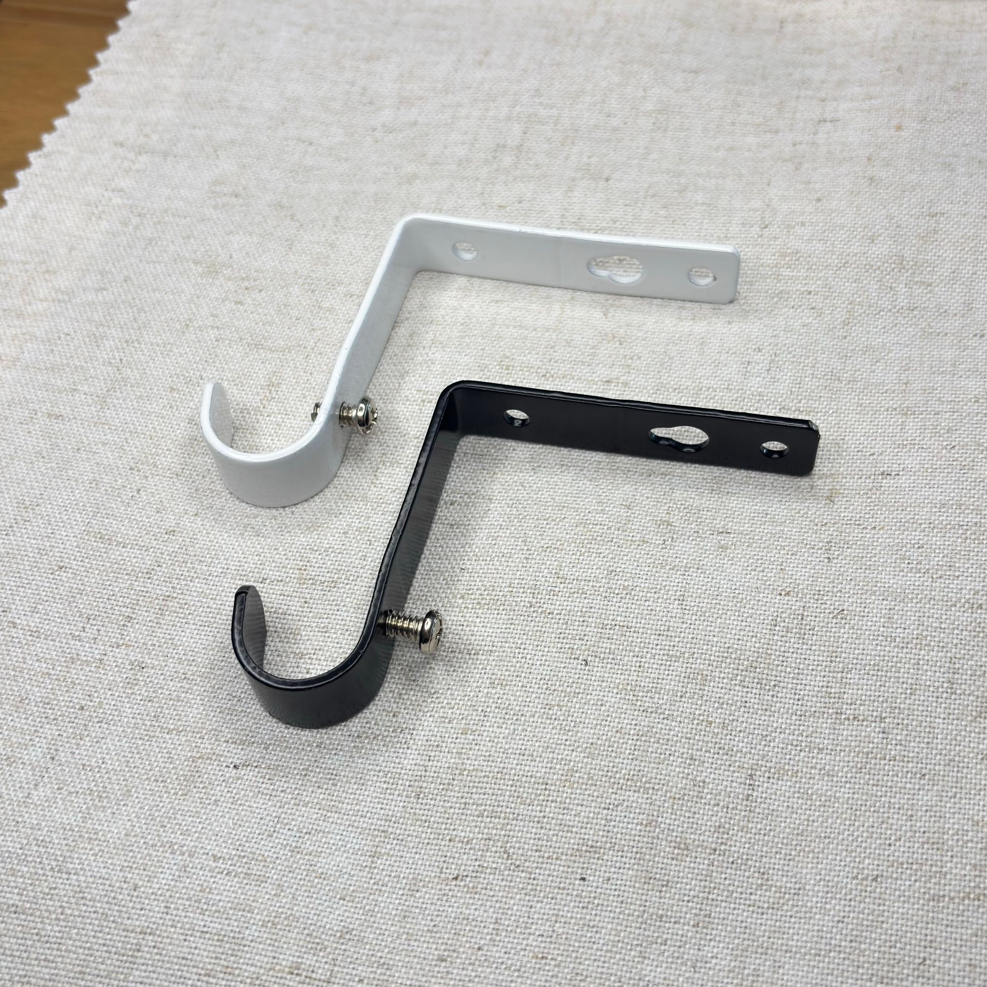 Soporte de barra de cortina de metal negro con tornillos y anclajes de pared sobre una superficie blanca.