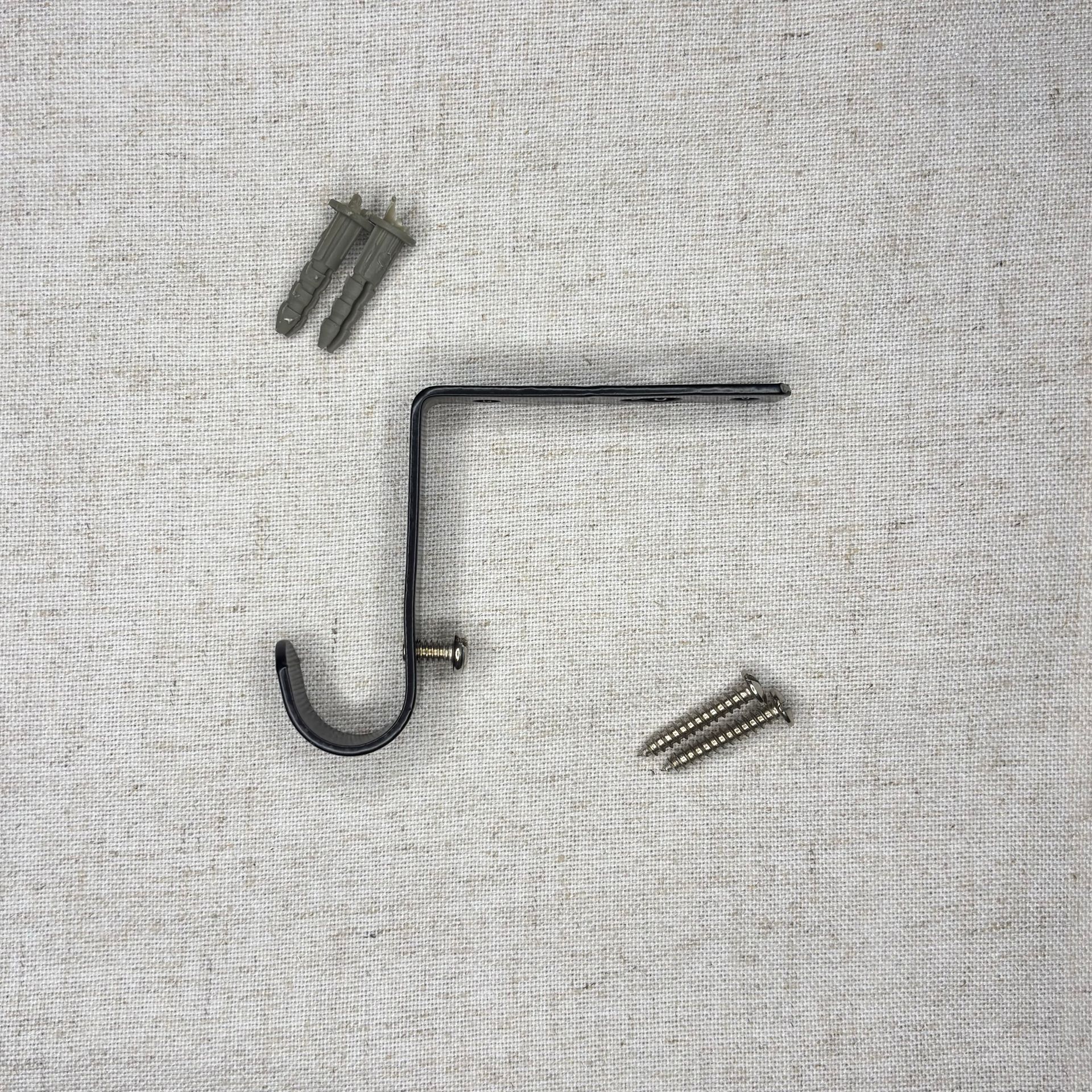 Soporte de barra de cortina de metal negro con tornillos y anclajes de pared sobre una superficie blanca.