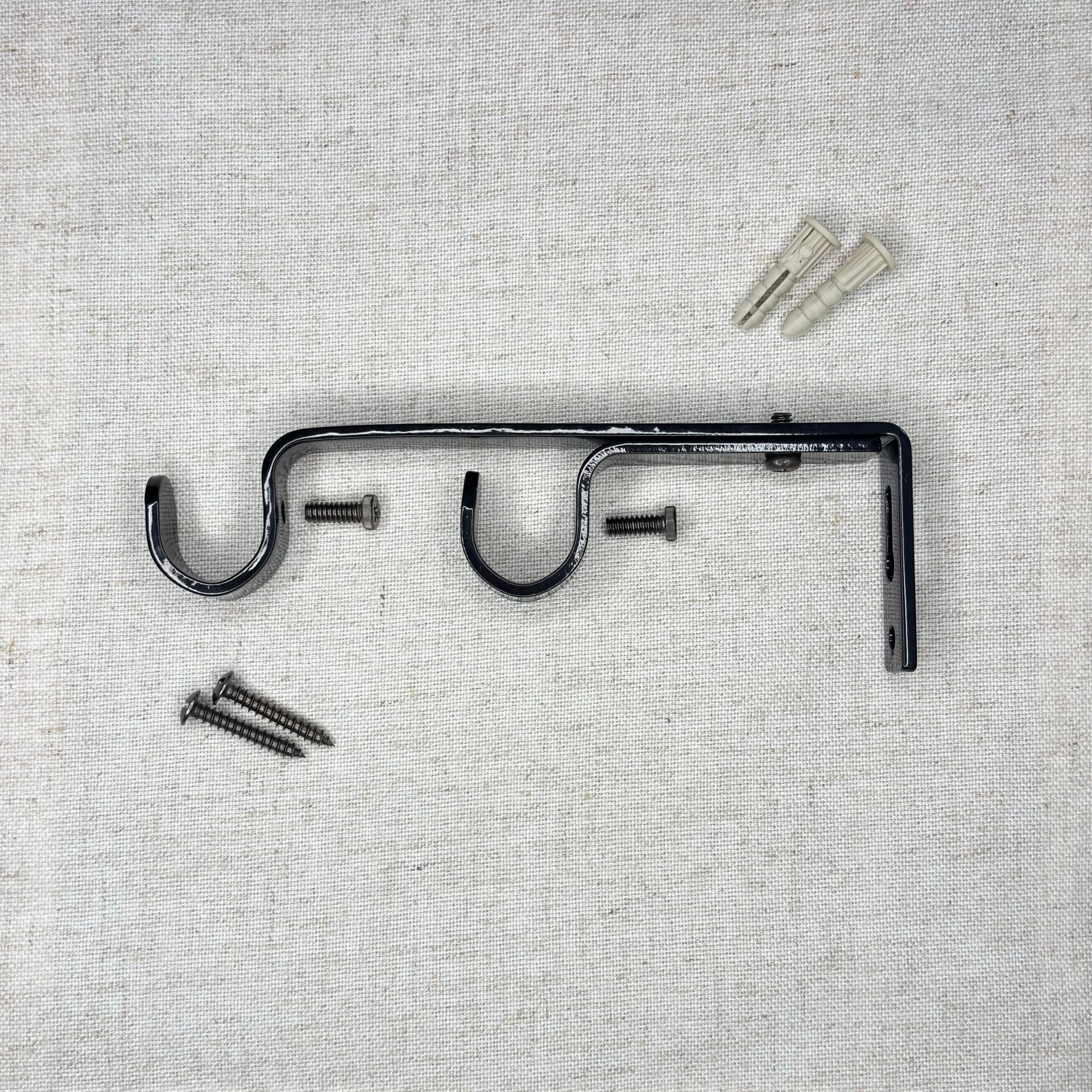 Soporte de barra de cortina doble negro con tornillos y anclajes de pared sobre una superficie texturizada blanca.