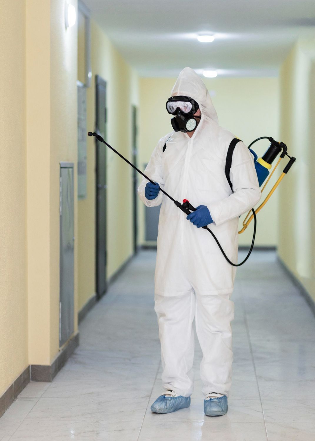 A man in a protective suit is spraying a wall in a hallway.