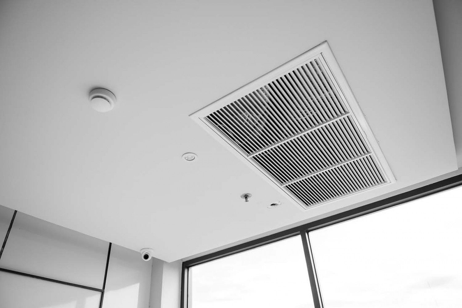 A black and white photo of a ceiling fan in a room with a window.