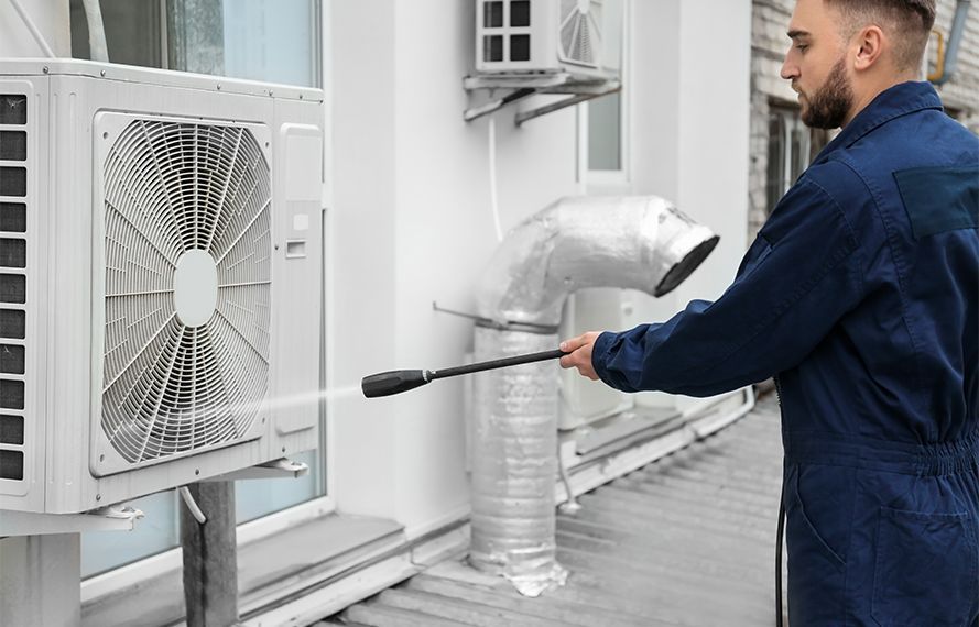 A man is cleaning an air conditioner with a high pressure washer.
