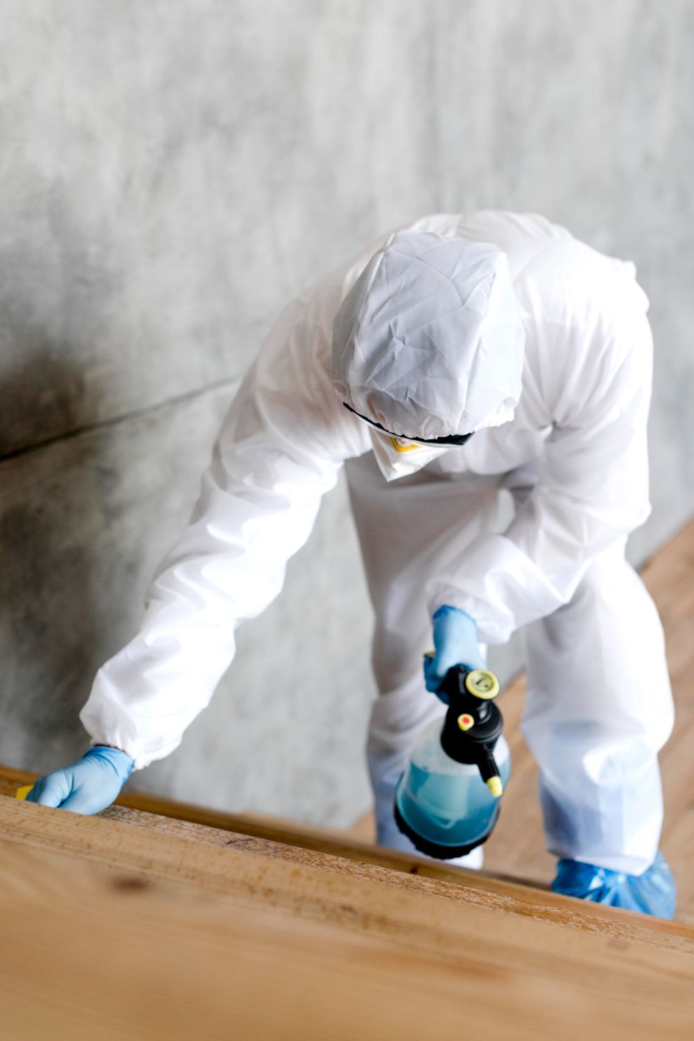 A man in a protective suit is spraying a wooden floor.