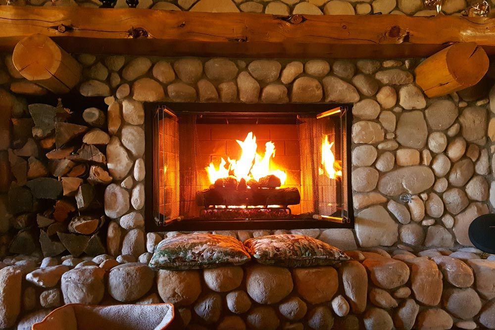 A fireplace with a glass screen surrounding it is lit up in a living room.