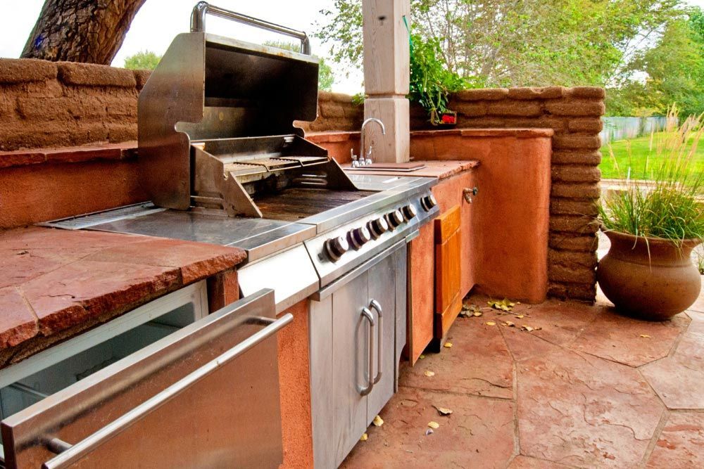 An outdoor kitchen with a grill and a refrigerator