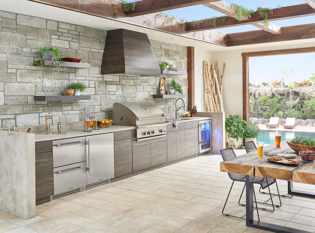 A large outdoor kitchen with a table and chairs and a stainless steel grill.