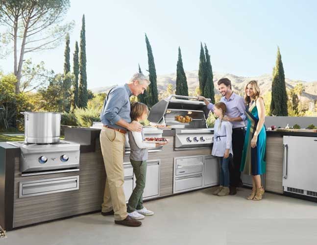 A family is standing in a kitchen looking at a grill.