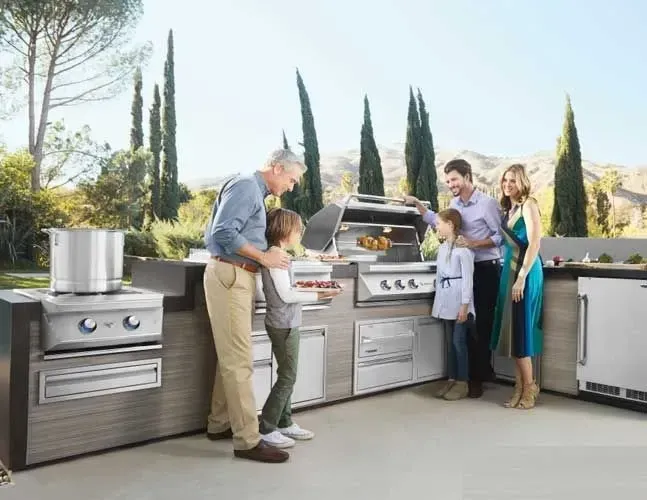 A family is standing in a kitchen looking at a grill.