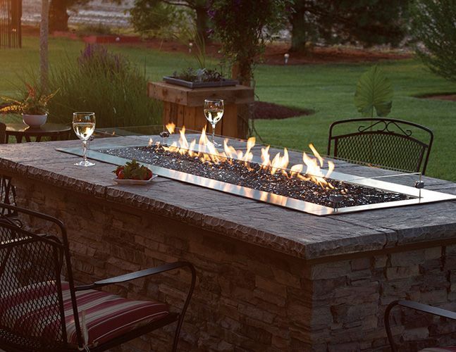 A table with a fire pit and two glasses of wine on it.