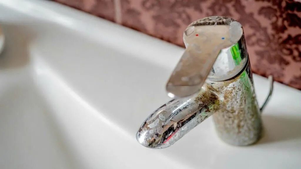 A chrome bathroom faucet covered in hard water mineral deposits, positioned over a white ceramic sink.