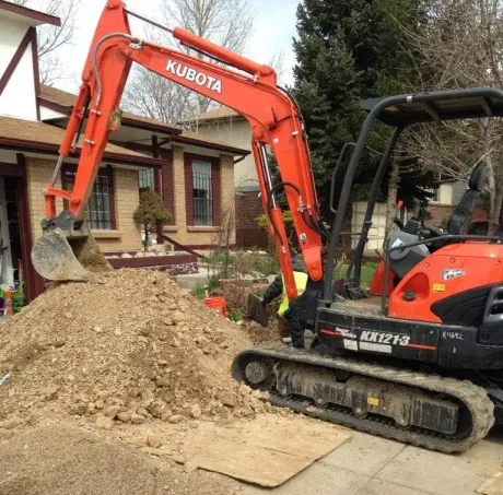 A bright orange Kubota KX121-3 mini excavator digging a hole in a residential yard near a house.