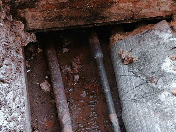 A close up of a pipe in the ground next to a brick wall.