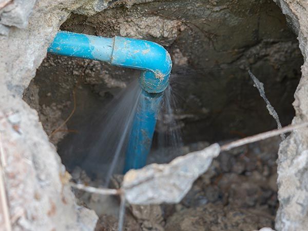 A blue pipe is leaking water in a hole in the ground.