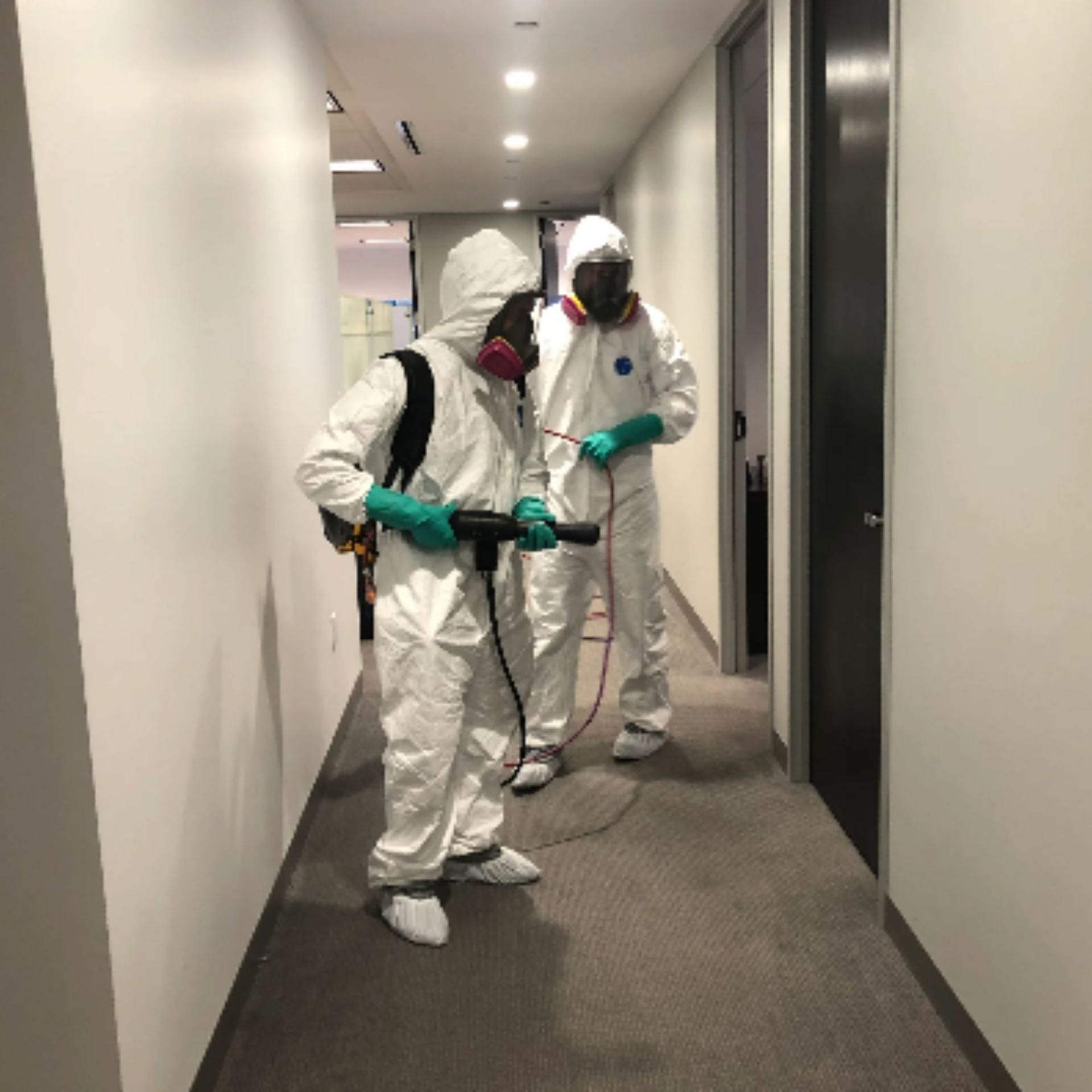Mold Remediation Inc -Two people in white suits are spraying a hallway