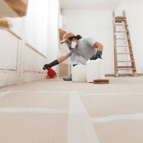 Mold Remediation Inc -A man wearing a mask is spraying something on the floor