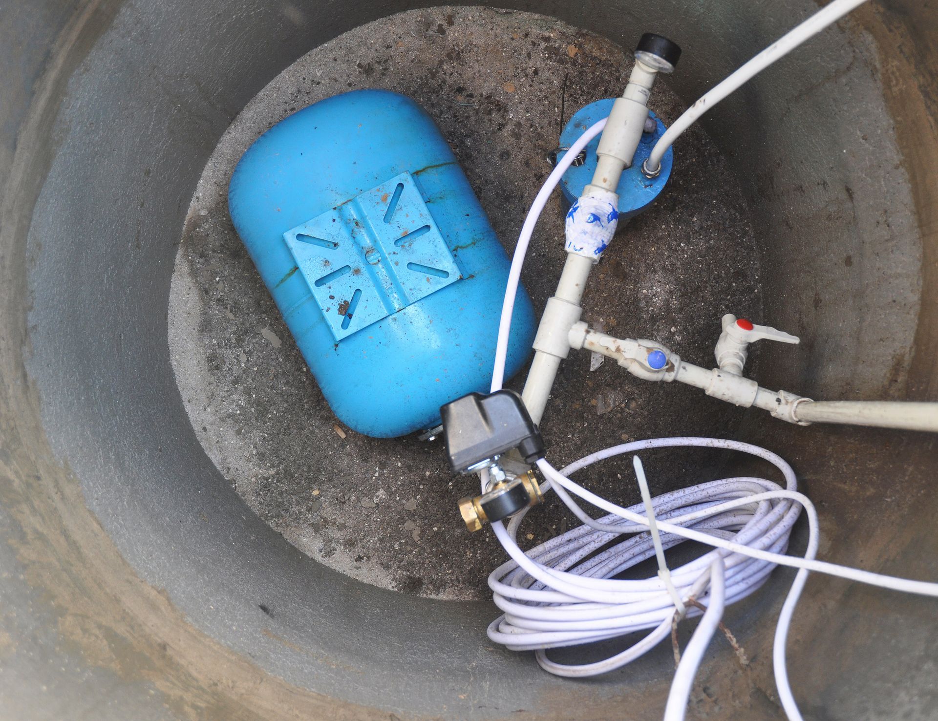 Blue water tank with plumbing inside a concrete well.