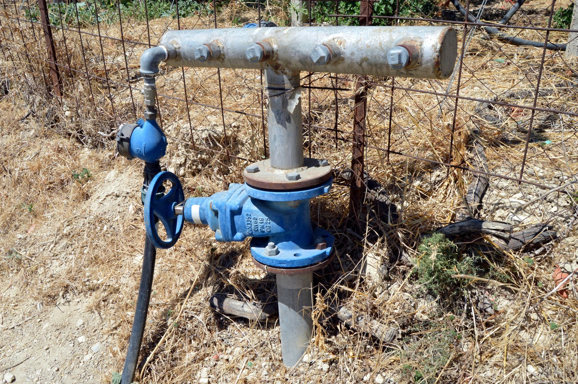 Water well with blue valve and metal piping in a dry, outdoor setting.