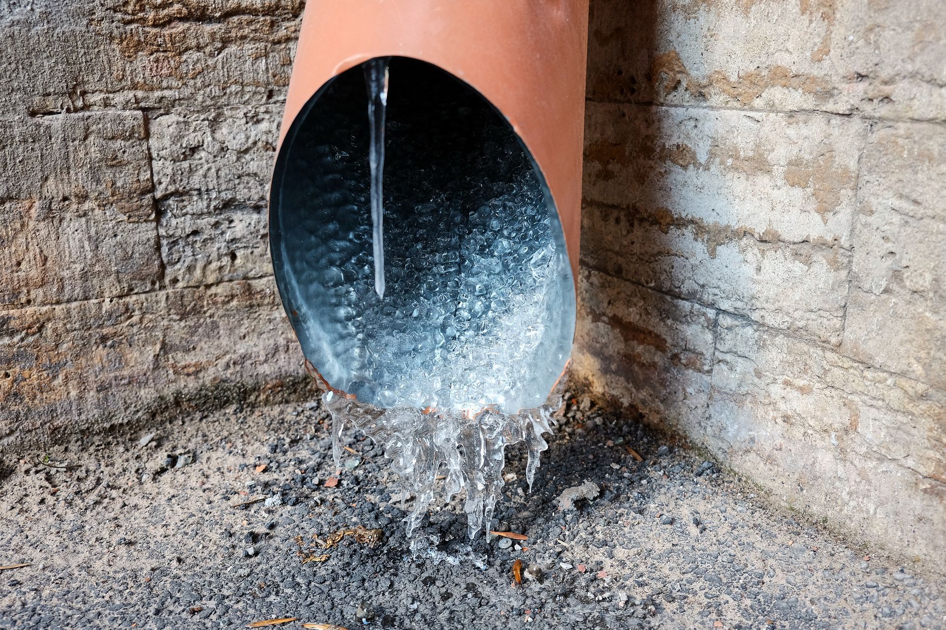 Water pouring from a brown, curved pipe against a brick and concrete wall.