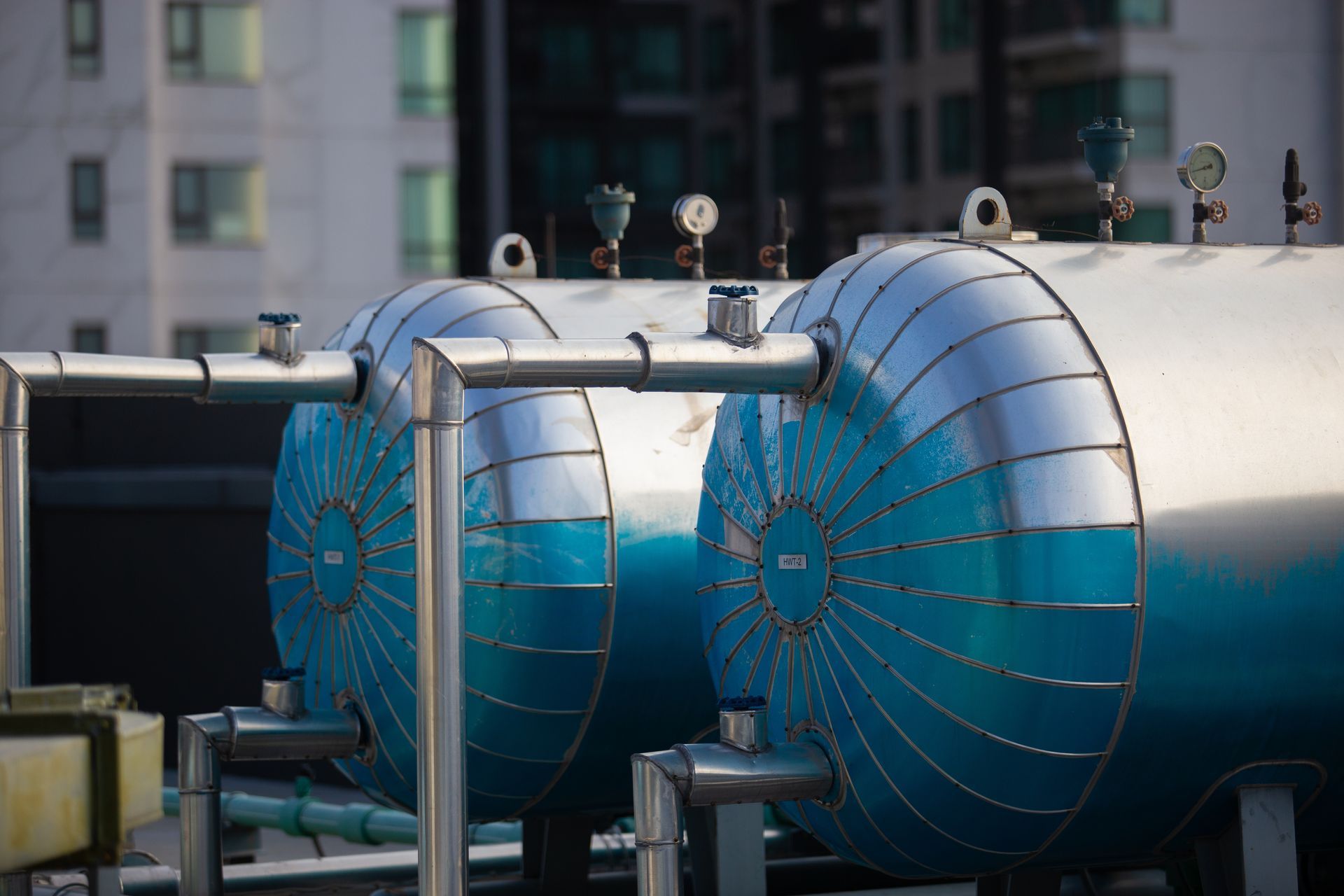 Two cylindrical blue and silver tanks with pipes and gauges on a rooftop.