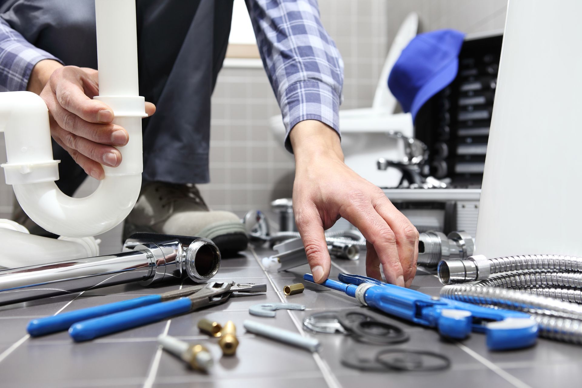 Plumber working on bathroom pipes, surrounded by tools and fittings on the floor.