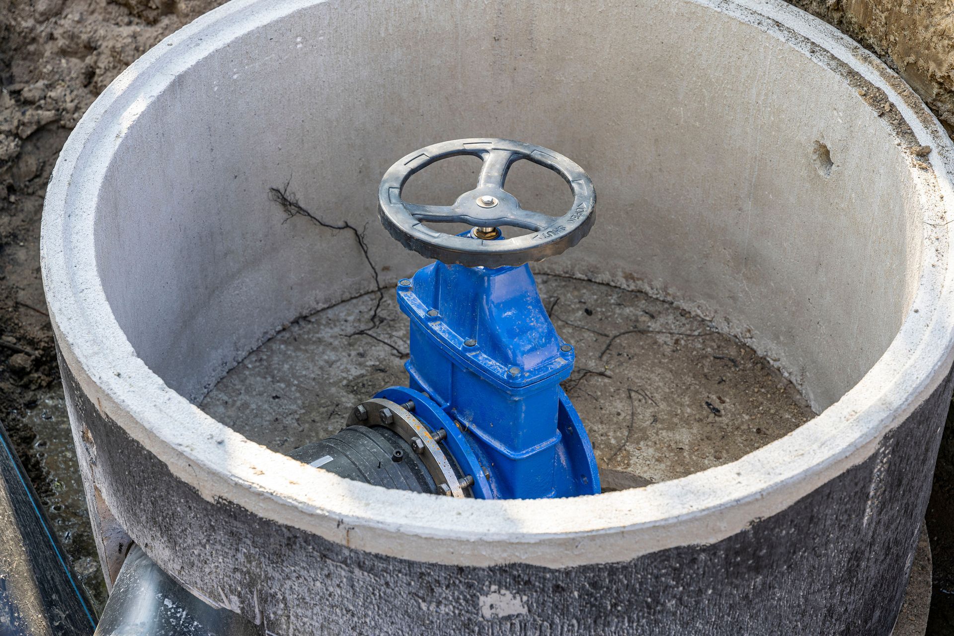Blue water valve inside a concrete manhole, handle in the upright position.