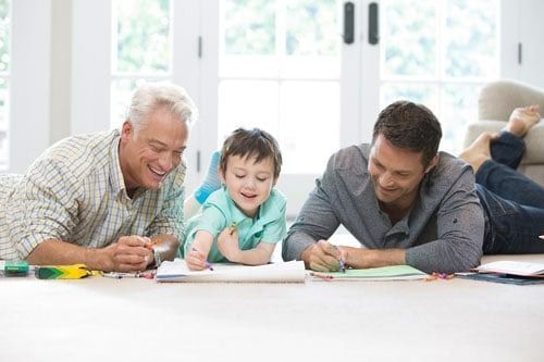 Three men are laying on the floor with a little boy.