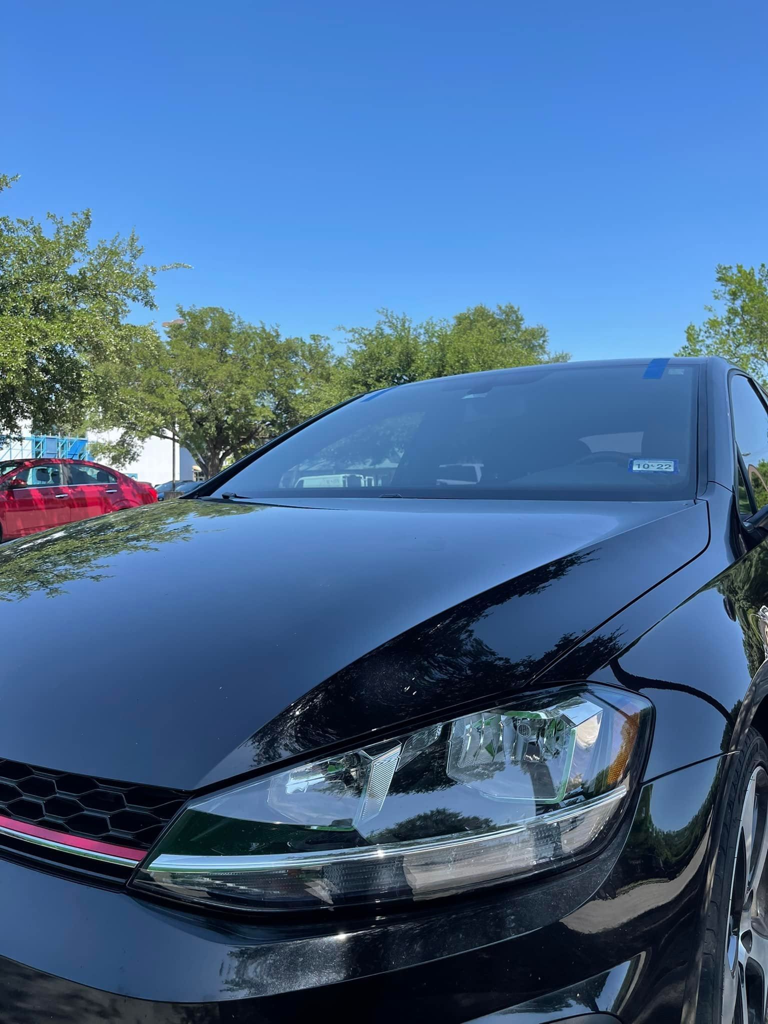 A black car is parked in a parking lot on a sunny day.
