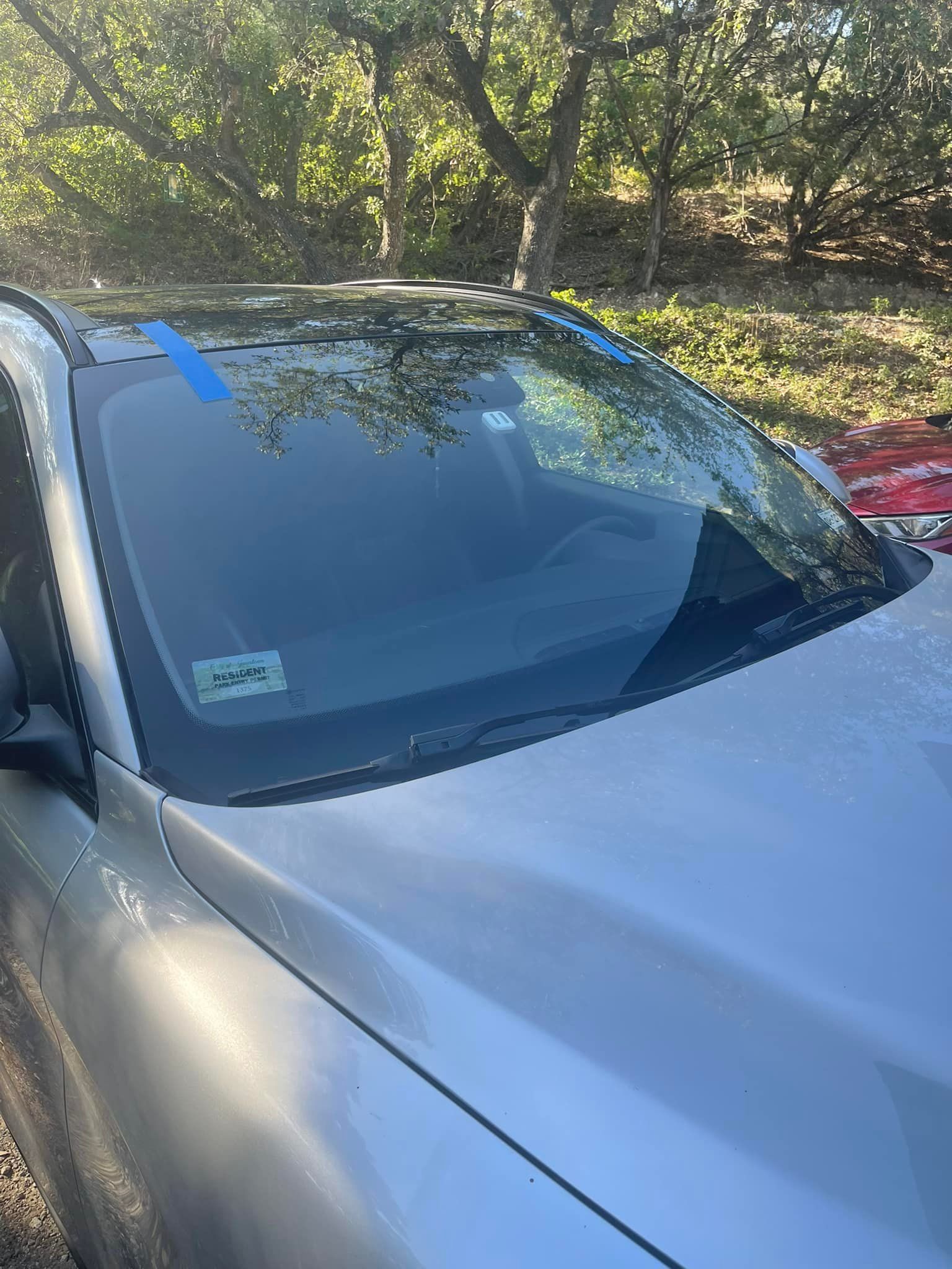 A silver car is parked in a parking lot with trees in the background.