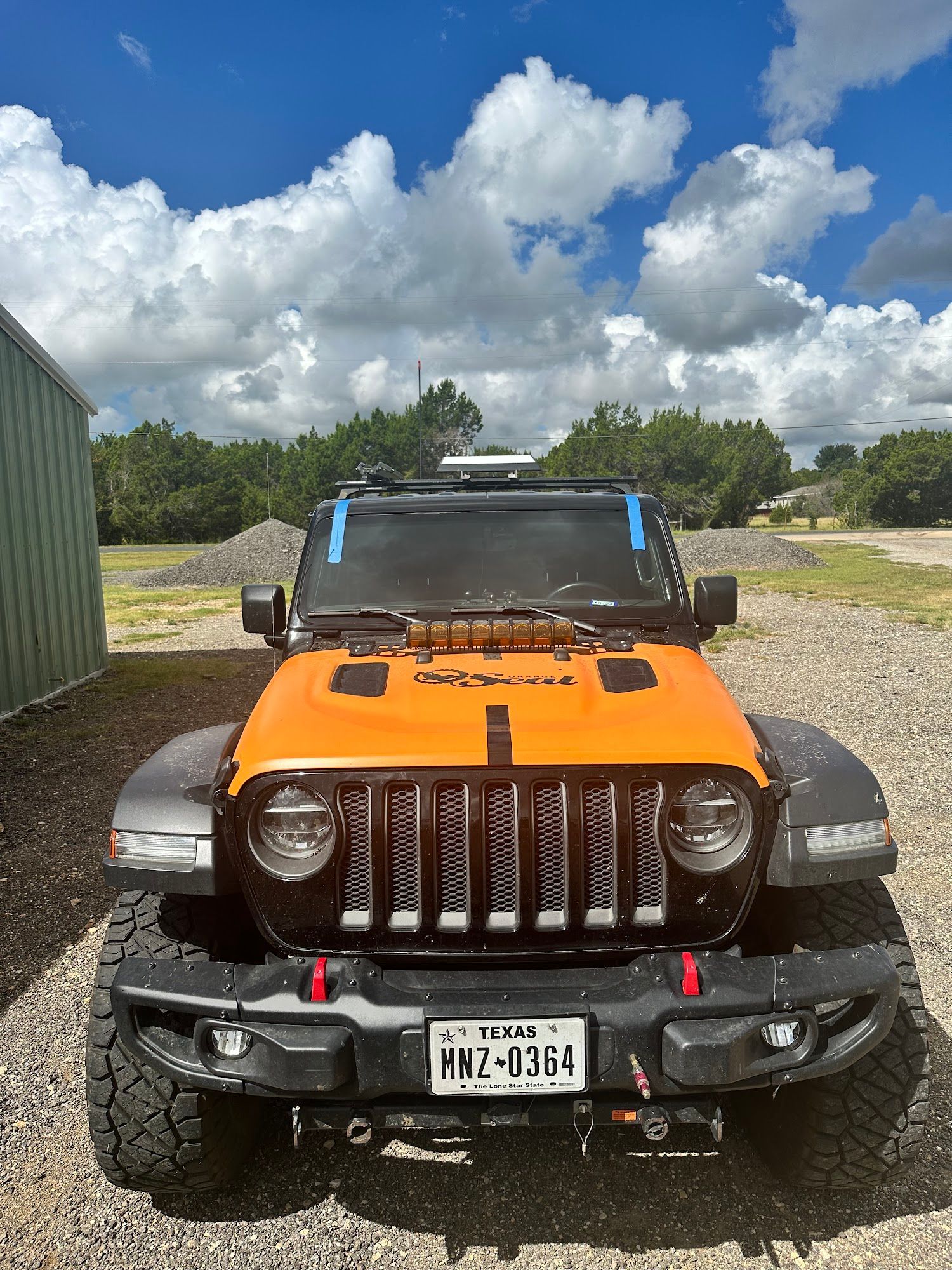 A jeep is parked in a gravel lot on a sunny day.