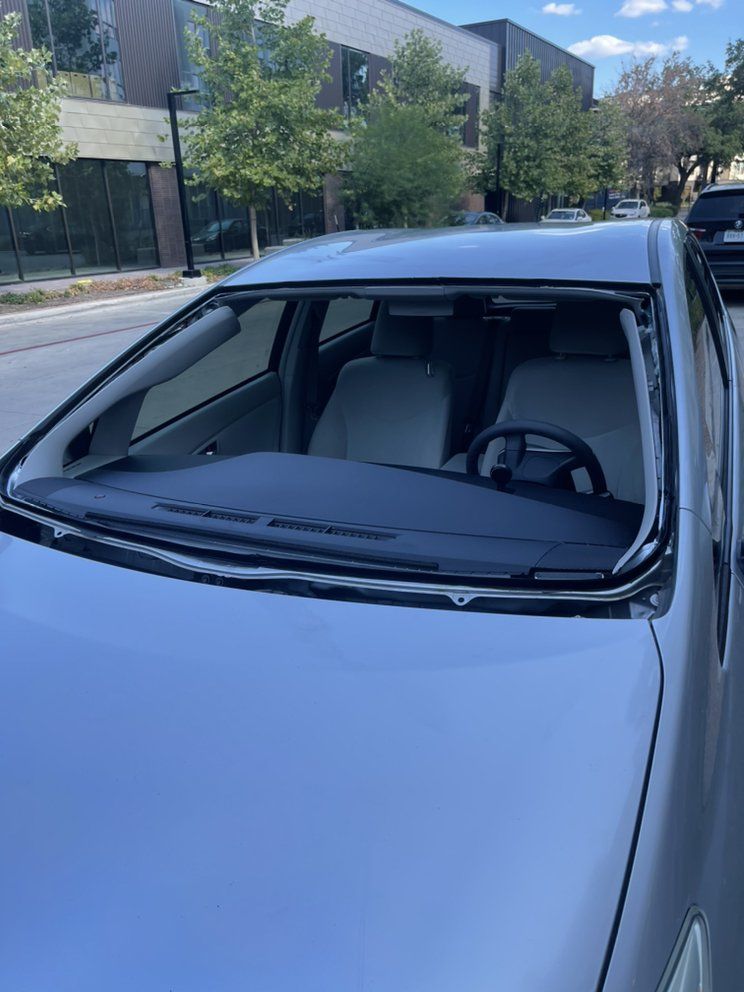 A silver car with a broken windshield is parked on the side of the road.