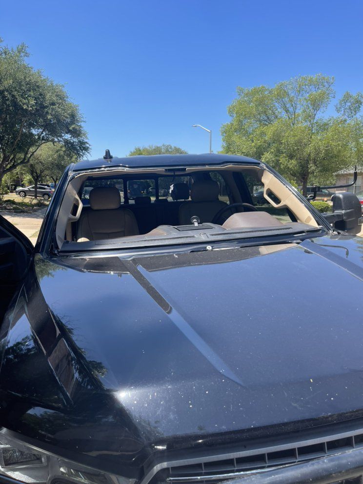 A black truck with a broken windshield is parked in a parking lot.