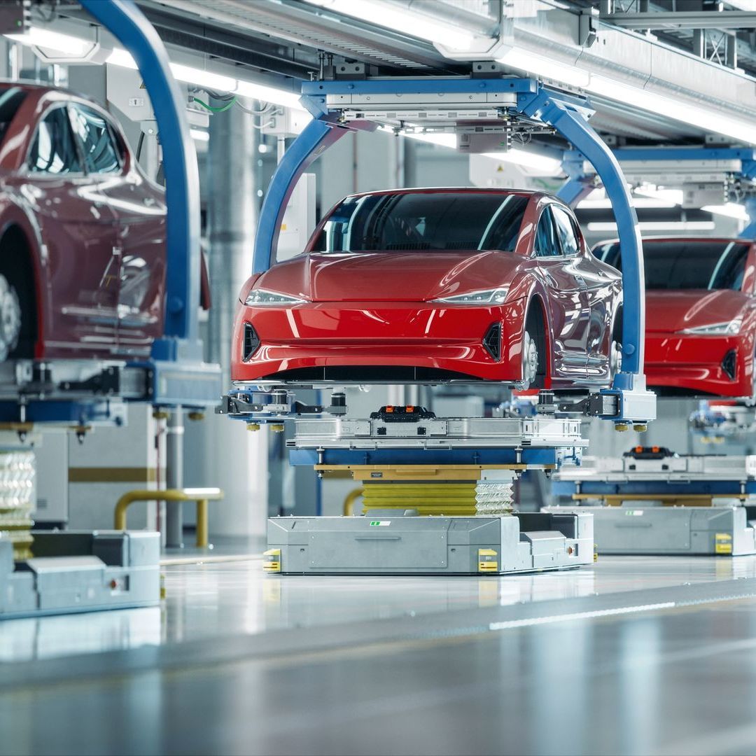 A row of red cars are sitting on a conveyor belt in a factory.