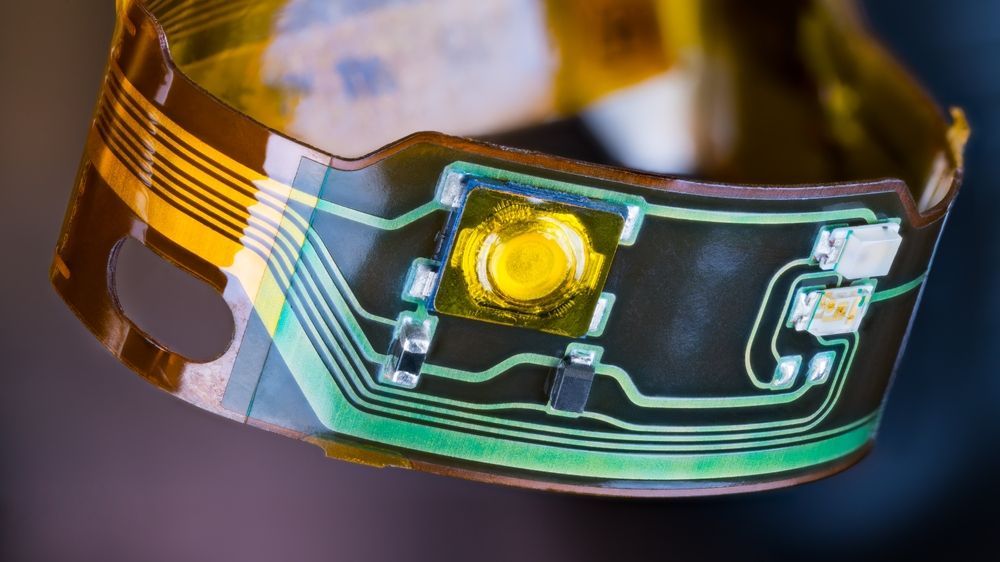 Close-up of a flexible amber circuit board with a yellow component and glowing green traces
